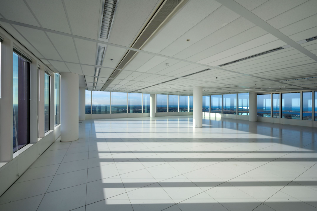 Lichte, lege kantoorruimte met witte vloer en grote ramen aan de P.J. Oudweg met uitzicht over de stad.